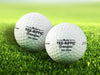 Two white Titleist golf balls with Tee-riffic Grandpa designs on top of golf course grass background