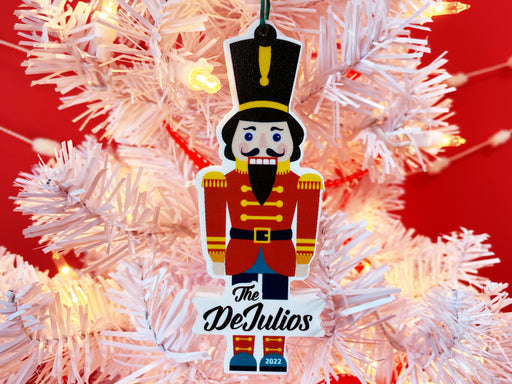Ornament shown hanging from Christmas tree. The ornament made from PVC and shaped like a nutcracker. A last name and year are written on the ornament.