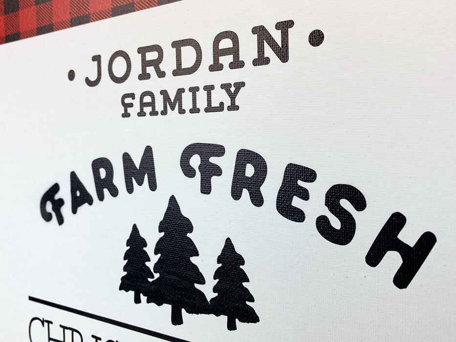 Closeup photo of canvas design. Farm Fresh Christmas Trees design shown on canvas. Design has red and black plaid border with black text, Jordan Family Farm Fresh Christmas Trees Hot Cocoa & Cider Served Daily.