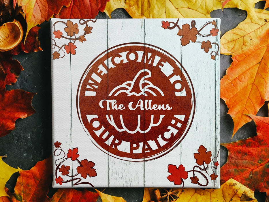 Printed canvas lays on surface with fall leaves. Canvas has design with pumpkin and pumpkin foliage on sides. Design says Welcome to Our Patch and The Allens.