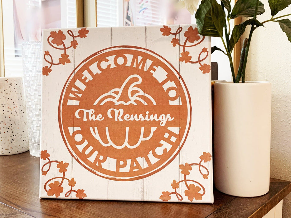 Printed canvas sits on tablescape. Canvas has design with pumpkin and pumpkin foliage on sides. Design says Welcome to Our Patch and The Rensings.