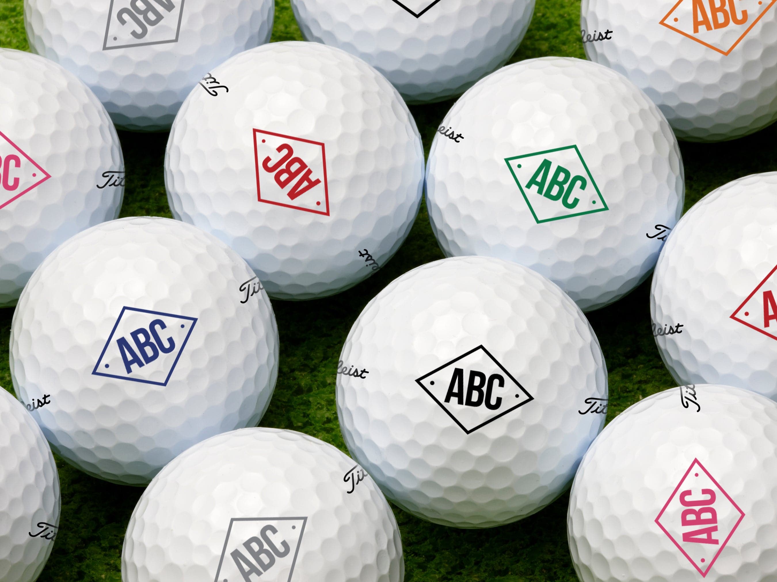 single white titleist golf ball on white golf tee with custom black diamond monogram design ABC printed on it against grass golf field background
