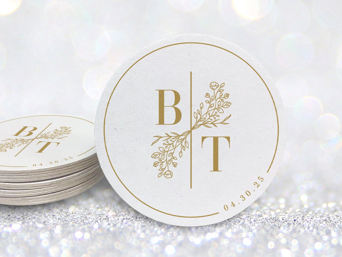 A stack of custom round coasters against a white background. Coasters feature a custom floral monogram design with two initials and floral decoration in the middle and a border with a wedding date on the side.