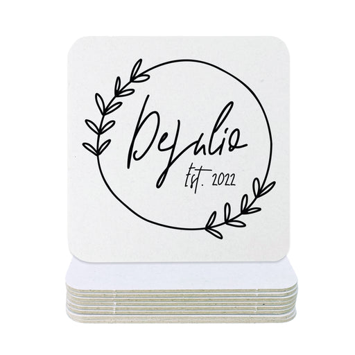 Single coaster is shown on top of a stack of coasters on a white background. Coasters feature Floral Family Name design. Design has a simple, circular, floral frame around the words "DeJulio Est. 2022". Design is printed on a white coaster.