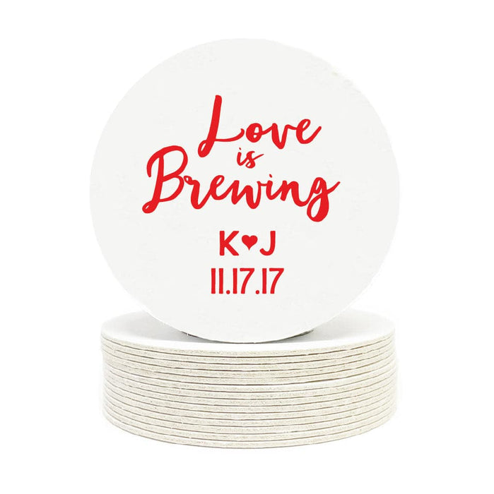Single coaster is shown on top of a stack of coasters on a white background. Coasters feature Love is Brewing design. The following text is shown on coasters: "Love is Brewing" in a brush script, the initials K and J with a heart between them, and the date, 11.17.17. This design is printed in red on white round coasters.