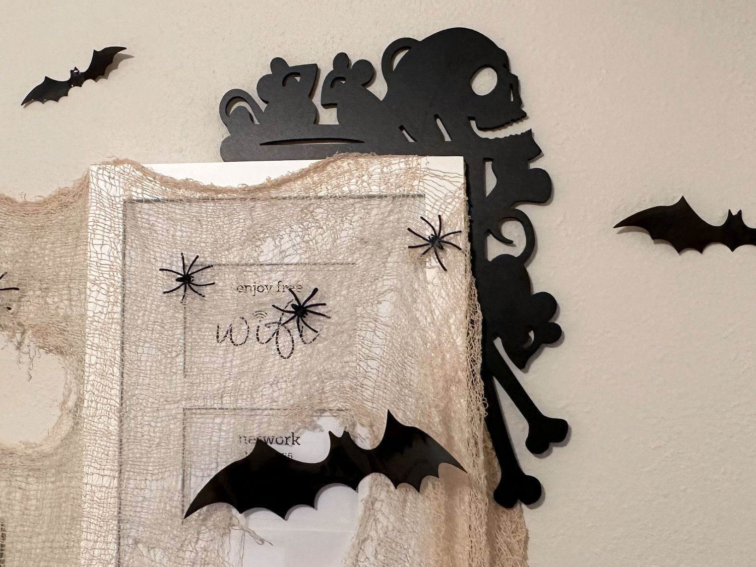 A black door frame topper, designed with the silhouette of scurrying rats, bones, and a skull, is seen on top of a white door frame. The beige wall behind has fake bats attached to it.