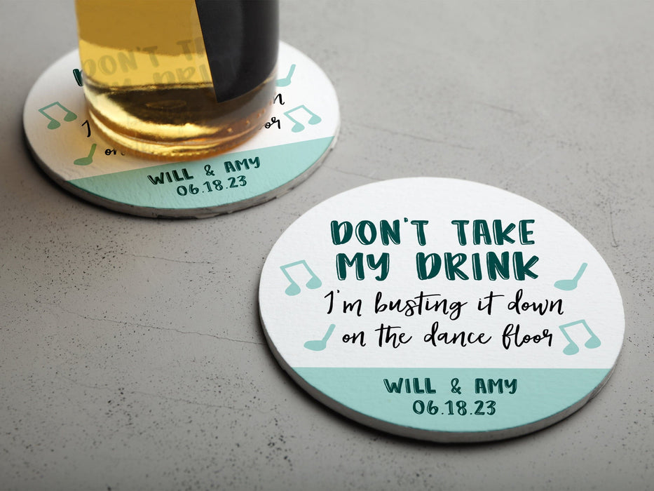 One coaster has a drink on it and an empty coaster sits beside it. Coasters say Don't take my drink, I'm busting it down on the dance floor. Married couple names are below with wedding date.