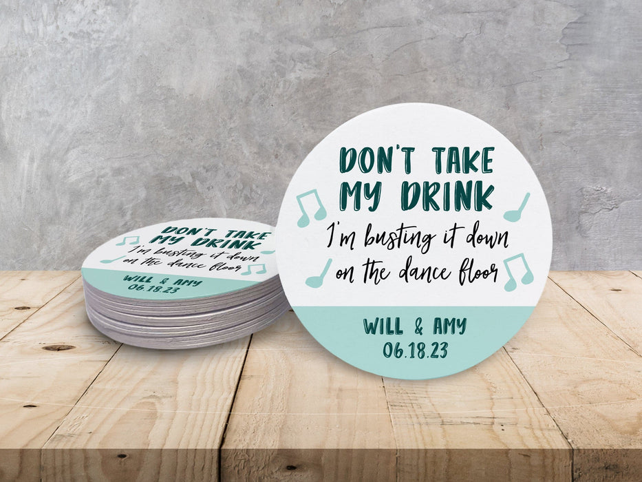 A stack of coasters by a single coaster on wooden table. Coasters say Don't take my drink, I'm busting it down on the dance floor. Married couple names are below with wedding date.