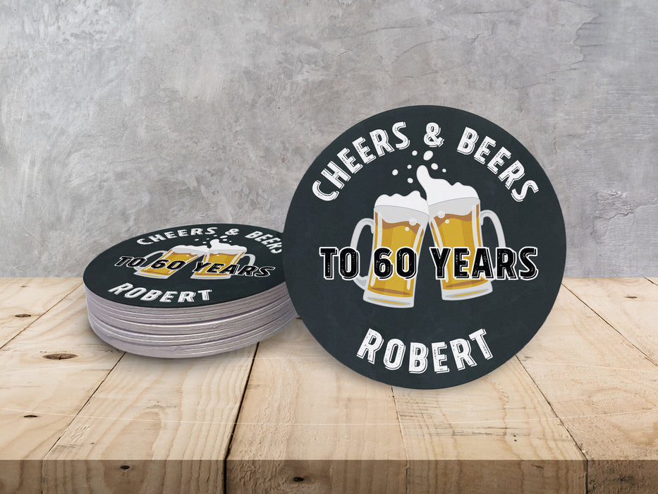 Stack of coasters with one on on the side on wooden table in front of gray wall. Coasters say Cheers & Beers to 60 Years Robert!