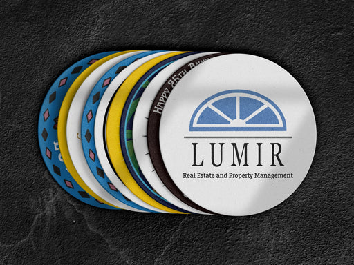 Stack of coasters spread out on black marble background. Coasters display all different custom designs and colors. The most visible coaster on top of the stack is a logo for a real estate and property management company.