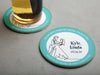 One coaster has a drink on it and an empty coaster sits beside it. Coasters say Please Don't Take My Drink, I'm Dancing in white around a teal border with an illustration of a married couple dancing beside their names and wedding date.