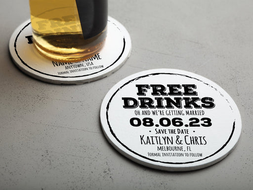 One coaster has a drink on it and an empty coaster sits beside it. Coasters feature Free Drinks Save the Date design. Design has a circular brushstroke around the text “Free Drinks, Oh And We’re Getting Married, 08.06.23, Save The Date, Kaitlyn & Chris, Melbourne, FL, Formal Invitation to Follow”. Design is printed in black on a white round coaster.