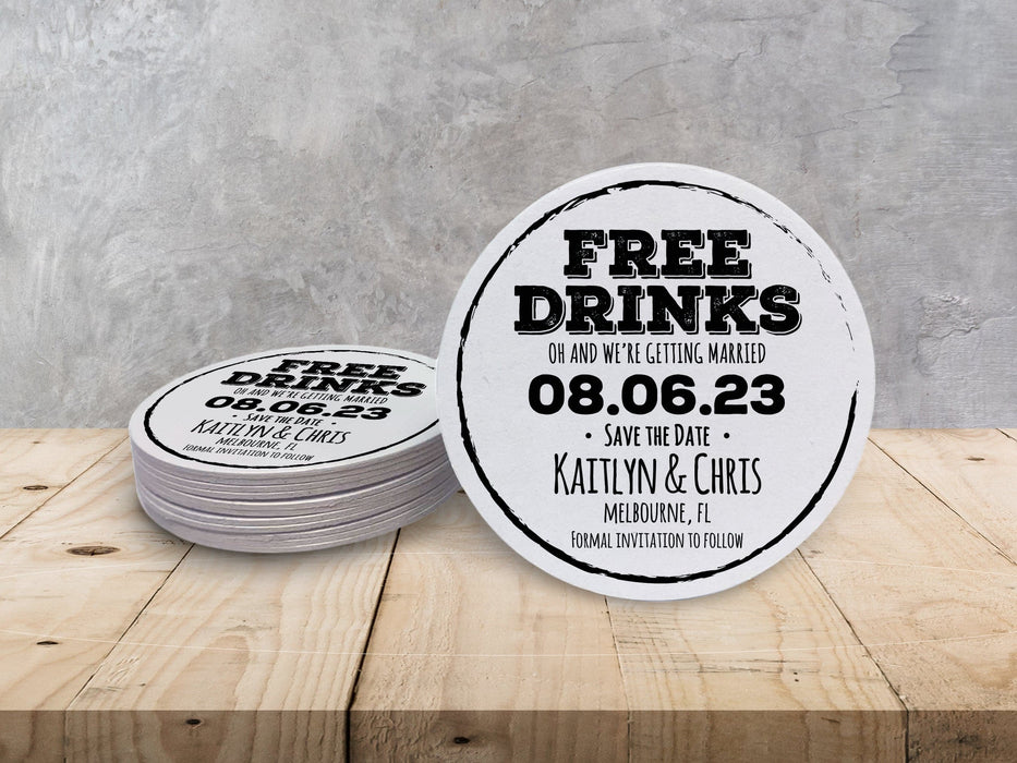 A stack of coasters by a single coaster on wooden table. Coasters feature Free Drinks Save the Date design. Design has a circular brushstroke around the text “Free Drinks, Oh And We’re Getting Married, 08.06.23, Save The Date, Kaitlyn & Chris, Melbourne, FL, Formal Invitation to Follow”. Design is printed in black on a white round coaster.