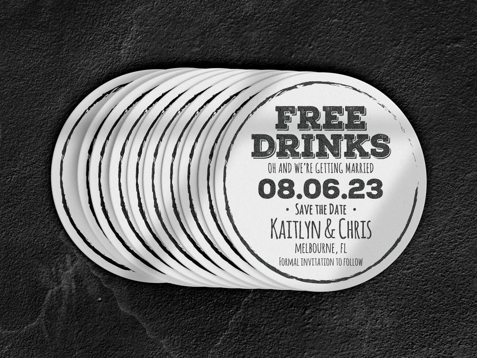 Stack of coasters spread out on black marble background. Coasters feature Free Drinks Save the Date design. Design has a circular brushstroke around the text “Free Drinks, Oh And We’re Getting Married, 08.06.23, Save The Date, Kaitlyn & Chris, Melbourne, FL, Formal Invitation to Follow”. Design is printed in black on a white round coaster.