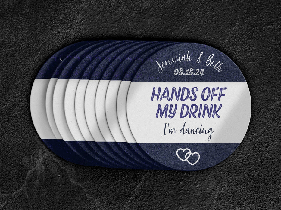 Stack of coasters spread out on black marble background. Coasters say married couple names, wedding date, HANDS OFF MY DRINK I'm dancing. Coaster design is printed in purple and black on a white coaster.