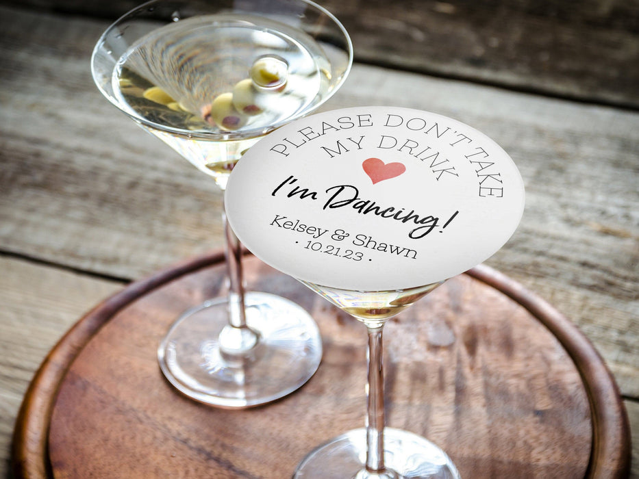 Personalized please don't take my drink coaster placed on top of martini glass on round wooden tray. Coaster has arched text with a red heart. Script I'm Dancing text in the middle with personalized text below.