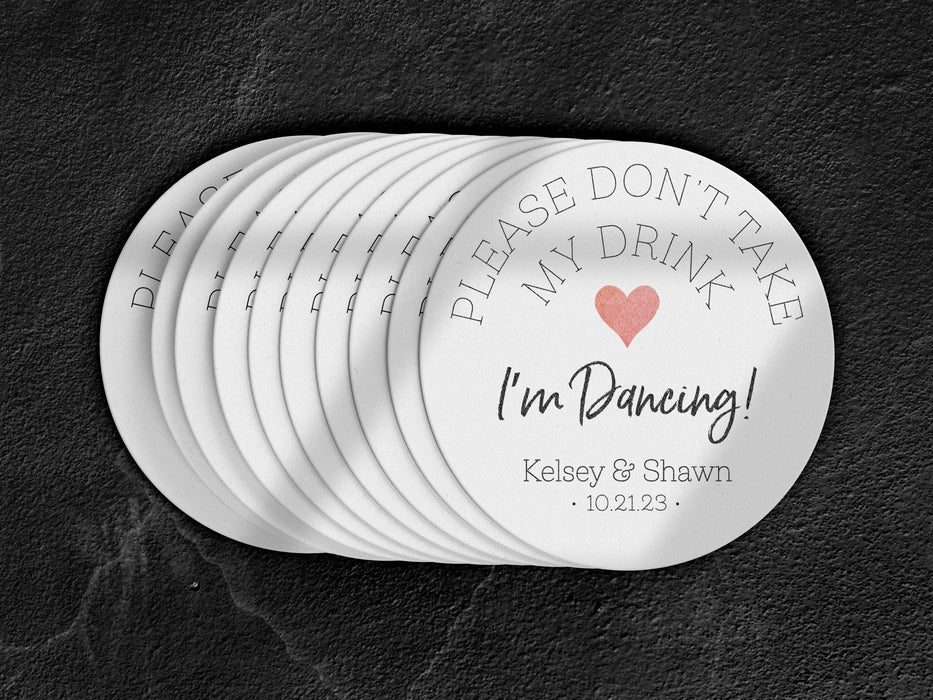 Stack of coasters spread out on black marble background. Coasters say please don't take my drink I'm dancing with married couple names and wedding date below. Red heart featured in the middle of coaster.