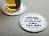 One coaster has a drink on it and an empty coaster sits beside it. Coasters say Please Don't Take My Drink I'm Dancing with wedding couple names and wedding date. The words, place on top of your drink while away, act as a border around coaster.