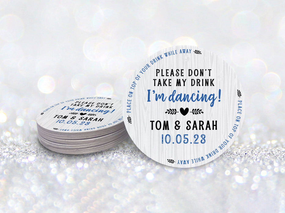 A stack of coasters by a single coaster in front of a glittery background. Coasters say Please Don't Take My Drink I'm Dancing with wedding couple names and wedding date. The words, place on top of your drink while away, act as a border around coaster.