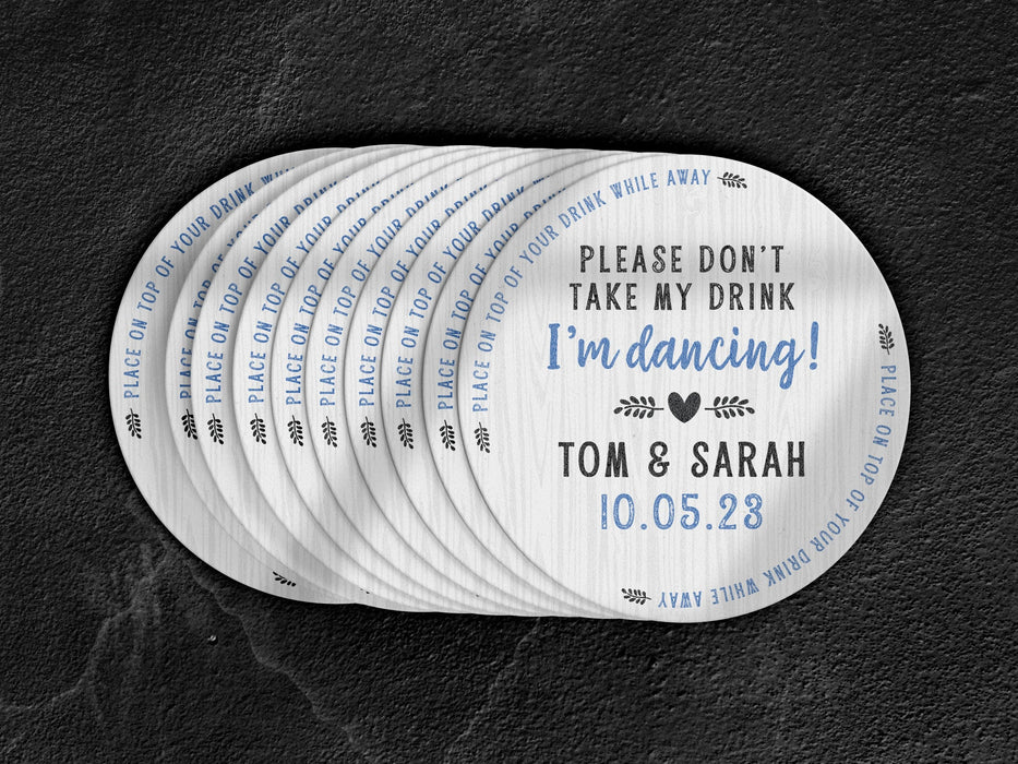 Stack of coasters spread out on black marble background. Coasters say Please Don't Take My Drink I'm Dancing with wedding couple names and wedding date. The words, place on top of your drink while away, act as a border around coaster.