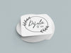 Stack of coasters sit on a gray background. Coasters feature Floral Family Name design. Design has a simple, circular, floral frame around the words "DeJulio Est. 2022". Design is printed on a white square coaster.