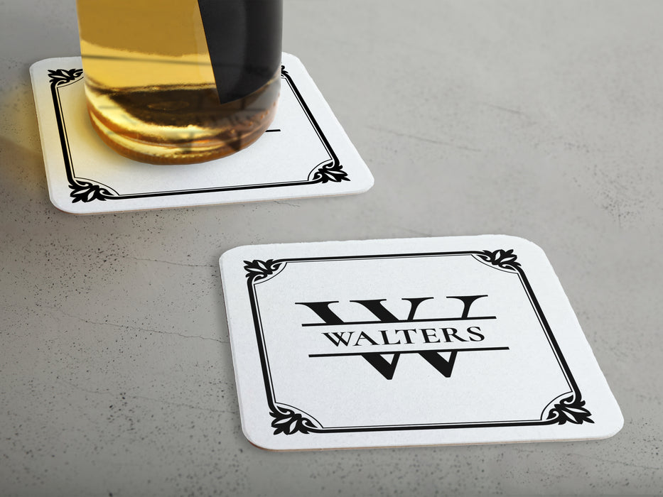 One coaster has a drink on it and an empty coaster sits beside it. Coasters feature Framed Monogram Family Name design. Design has a square ornamental frame around a monogram for the last name "Walters". Design is printed on a white coaster.