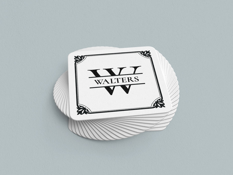 Stack of coasters sit on a gray background. Coasters feature Framed Monogram Family Name design. Design has a square ornamental frame around a monogram for the last name "Walters". Design is printed on a white coaster.