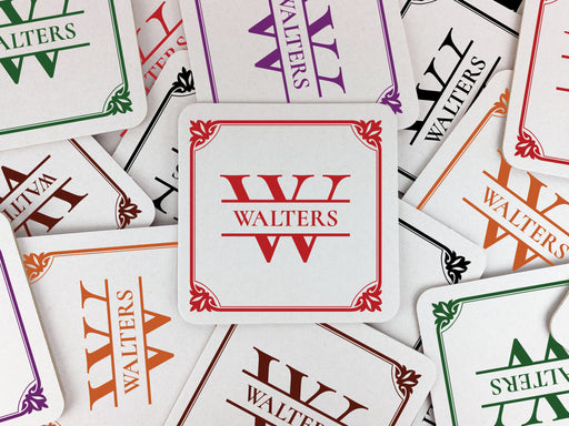 Multiple coasters shown in the following colors: Black, Brown, Green, Orange, Purple, and Red. Coasters feature Framed Monogram Family Name design. Design has a square ornamental frame around a monogram for the last name "Walters". Design is printed on a white coaster.