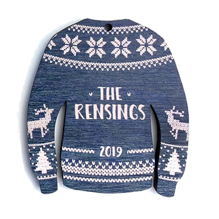 Ornament features an Ugly Sweater design. Design is navy and made in a sweater shape with white stitched decorative details. Decorative reindeer and Christmas trees are on sleeves. Custom last name and year are printed in white in the center.