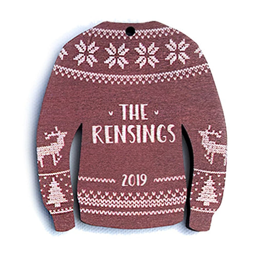 Ornament features an Ugly Sweater design. Design is red and made in a sweater shape with white stitched decorative details. Decorative reindeer and Christmas trees are on sleeves. Custom last name and year are printed in white in the center.