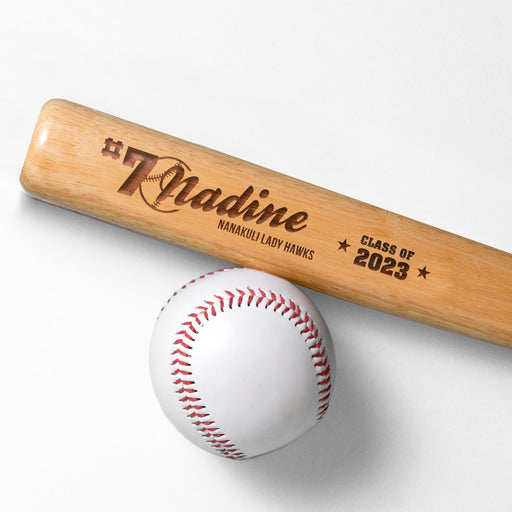 wooden mini baseball bat with custom laser engraved design that features a name with a baseball with a number and says "#7 Nadine, Nanakuli Lady Hawks, class of 2023" on a white surface next to a baseball