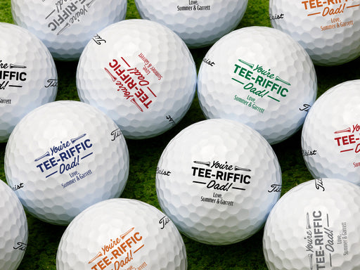 Multiple white titleist golf balls with Tee-riffic Dad design in all available color options on golf course grass
