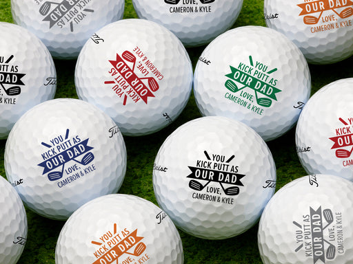 Multiple white titleist golf balls with Kick Putt Dad design in all available color options on golf course grass