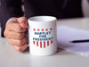 Business man holding white mug with red white and blue American design with typography that says Bartlet for president with Stars and Stripes on white table with paperwork and pen