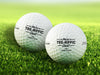 Two white Titleist golf balls with Tee-riffic Dad designs on top of golf course grass background