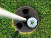Single white titleist golf ball with first Father's Day footprint design in golf course hole next to pole surrounded by grass