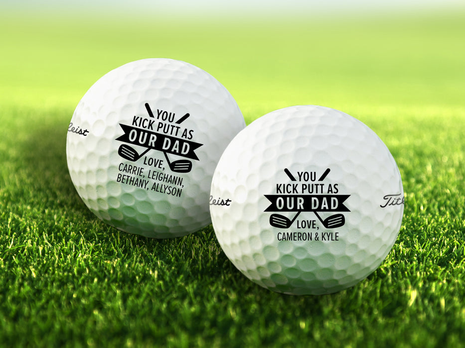 Two white Titleist golf balls with Kick Putt Dad designs on top of golf course grass background