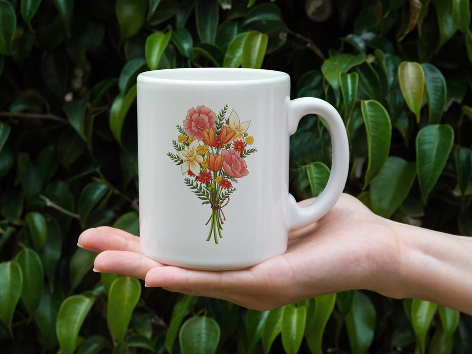 hand holding a 15 ounce ceramic mug featuring artwork of a bouquet of pastel spring flowers in front of outdoor leaves