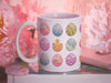 15 oz white ceramic mug with an easter pattern of floral decorated eggs with a baby chick popping out of an egg on a book surrounded by pink items such as a wallet, a pendant, and a flower
