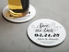 One coaster has a drink on it and an empty coaster sits beside it. Coasters say Save the Date, wedding date, married couple names, and formal invitation to follow.