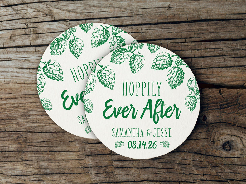 Two coasters are shown stacked on top of each other on wood table. Coasters feature Hoppily Ever After design. This design uses green lettering and sketched drawings of beer hops. Wedding couples names and date can be customized.