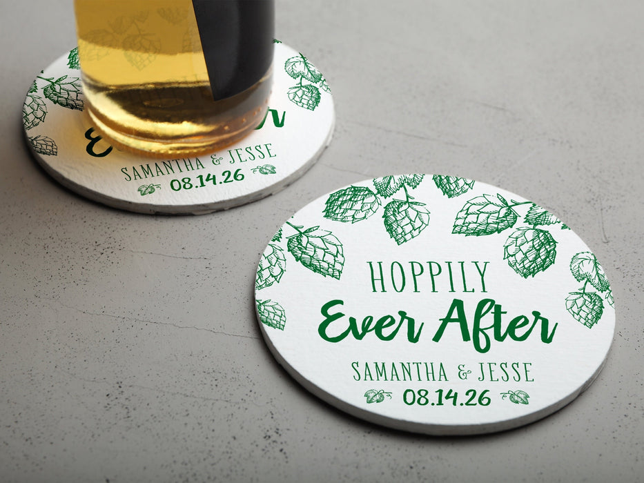 One coaster has a beer glass on it and an empty coaster sits beside it. Coasters feature Hoppily Ever After design. This design uses green lettering and sketched drawings of beer hops. Wedding couples names and date can be customized.