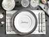A nice wedding table setting is shown with a coaster in the center. Coaster features Formal Last Name and Established Date design. This design has a white background and the happy couples last name and wedding year in emerald green writing.