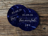 Two coasters are shown stacked on top of each other on wood table. Coasters feature Love Never Fails design. This design has a dark blue marble background and the happy couples first name initials and wedding date in white writing.