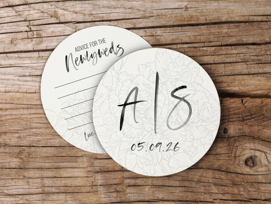 Two coasters are shown stacked on top of each other on wood table. Coasters show the front and back of the Floral Initial design. This design uses black ink on both sides with floral line art and brush script text.