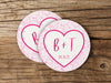 Two coasters are shown stacked on top of each other on wood table. Coasters feature Heart and Lace design. These are designed with the bride and groom first name initials and wedding date surrounded by a hot pink heart outline and light pink lace.