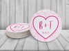 A stack of coasters by a single coaster on white wooden background. Coasters feature Heart and Lace design. These are designed with the bride and groom first name initials and wedding date surrounded by a hot pink heart outline and light pink lace.