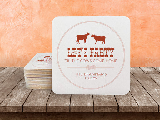 A stack of coasters by a single coaster on a wooden table. Coasters feature Til The Cows Come Home design. Design shows two cows with the saying Lets Party Til The Cows Come Home with newlyweds last name and wedding date.