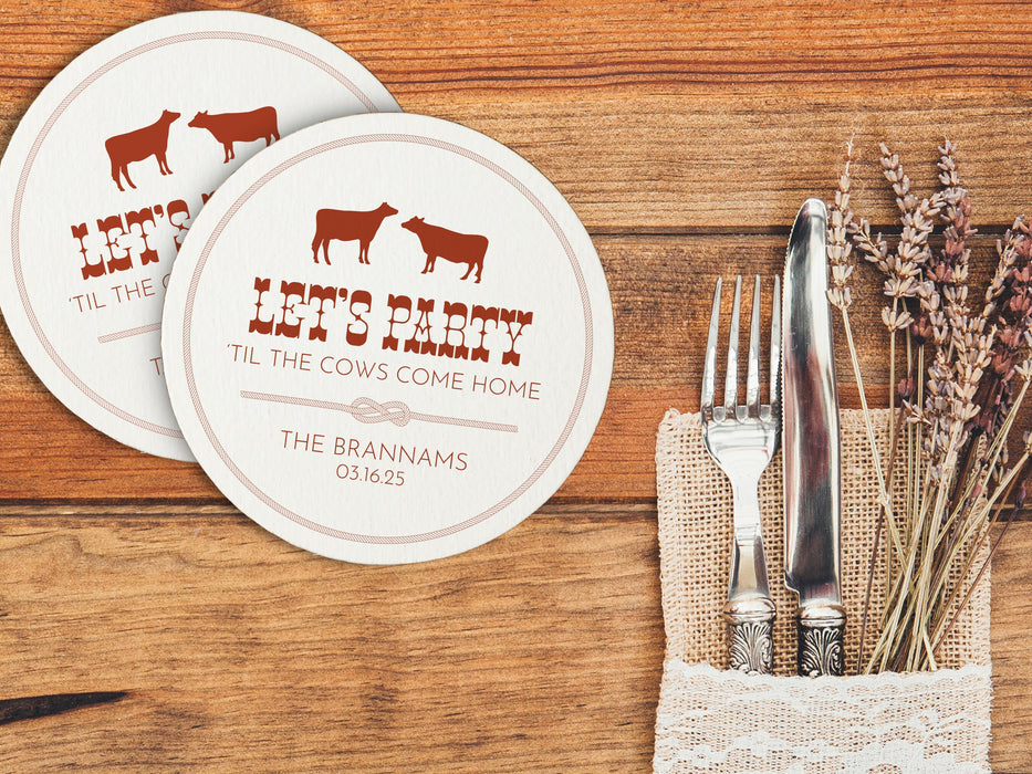 Two coasters are shown with a place setting against a light wood background. Coasters feature Til The Cows Come Home design. Design shows two cows with the saying Lets Party Til The Cows Come Home with newlyweds last name and wedding date.