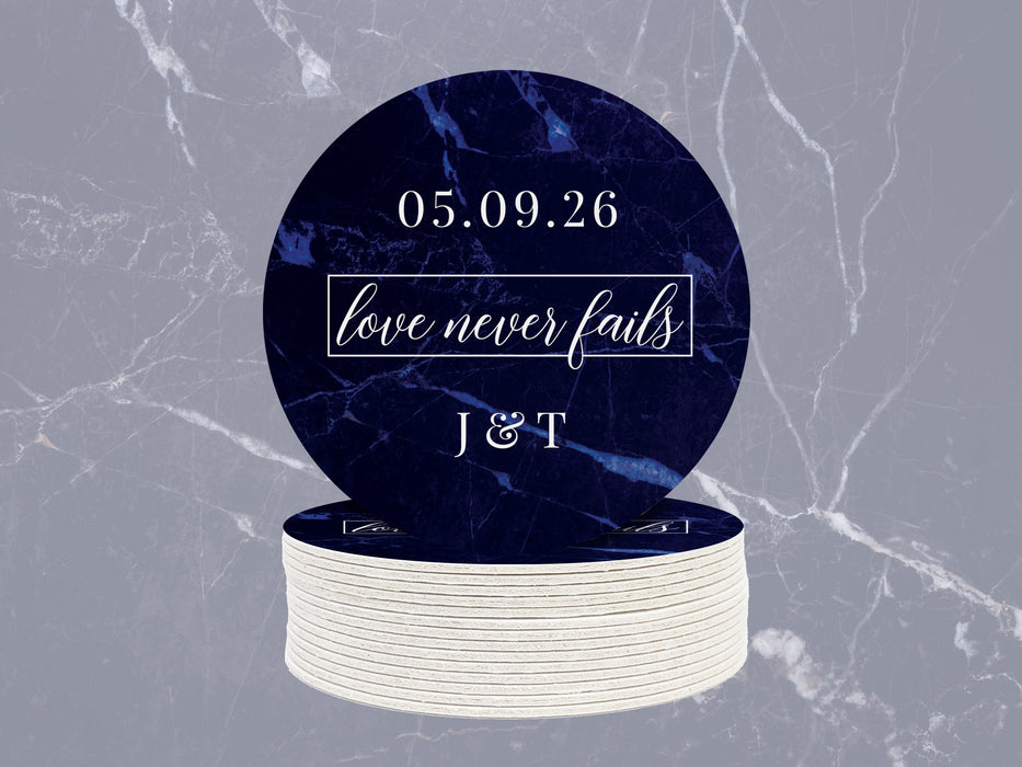 A stack of coasters with one on top is shown against a light blue marble background. Coasters feature Love Never Fails design. This design has a dark blue marble background and the happy couples first name initials and wedding date in white writing.